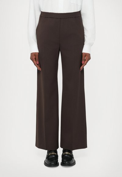 Pantaloni a gamba larga marroni con vita elastica, realizzati in tessuto morbido. Abbinati a mocassini neri con dettagli in hardware dorato.