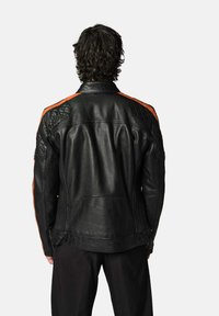 Veste de moto en cuir noir avec des accents en losange et des rayures orange sur les épaules, présentant une texture lisse et une coupe ajustée.