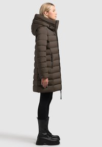 Brun puffig jacka med huva, dragkedja fram, och sidofickor, med ett quiltat mönster. Till den används svarta leggings och kraftiga snörstövlar.