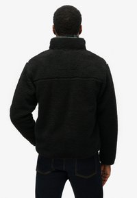 Zwarte fleece trui met hoge kraag en gestructureerde stof. Heeft een rechte zoom en wordt gecombineerd met donkere jeans, met minimale naden zichtbaar.