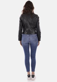 Giacca di pelle nera con un design aderente, abbinata a jeans skinny in denim blu. Sneakers bianche con dettagli neri completano il look.