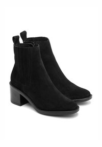 Czarne zamszowe botki za kostkę mają spiczasty nos, elastyczne panele boczne oraz stonowany obcas. Gładka tekstura z czystym, minimalistycznym designem.