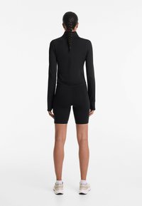 Top nero a maniche lunghe con colletto alto, abbinato a pantaloni corti da biker neri aderenti. Texture liscia con un design elegante e minimalista.