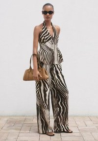 Zebramuster-Haltertop und weit geschnittene Hose in Braun und Creme, kombiniert mit einer kleinen braunen Tasche und schwarzen Sonnenbrillen. Flache Sandalen runden den Look ab.