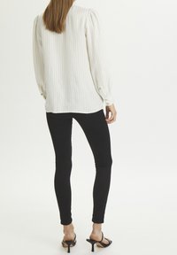 Weiß gestreifte Bluse mit puffartigen langen Ärmeln, geknöpften Manschetten, kombiniert mit schwarzen Slim-Fit-Jeans und schwarzen Absatzsandalen.