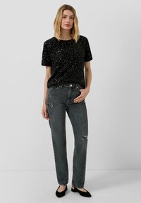 Czarna t-shirt z cekinami i krótkim rękawem w parze z ciemnymi dżinsami z przetarciami. Modelka ma na sobie czarne baleriny.