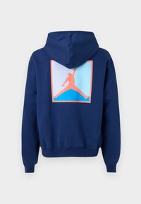 Námořnická modrá mikina s kapucí s velkým, barevným logem Jumpman umístěným na zadní straně, se geometrickým vzorem v růžové a modré.