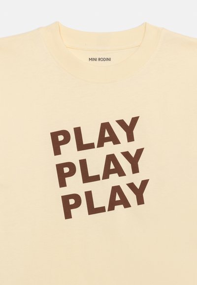 Μπεζ πουκάμισο με καφέ κείμενο "PLAY" επαναλαμβανόμενο τρεις φορές διαγώνια, στρογγυλή λαιμόκοψη, ετικέτα μάρκας Mini Rodini μέσα στο γιακά.