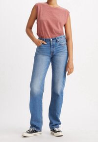 Camisa sin mangas roja, jeans de tiro alto de color azul claro y zapatillas de lona negras con suelas blancas. Los jeans tienen un corte relajado y un ligero desgastado.