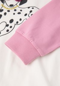 Lichtroze manchet met ribbelstructuur bevestigd aan een witte top met een zwart-wit dalmatiërprint ontwerp en gouden accenten.