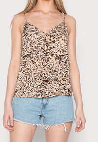 Top a spaghetto di colore beige con motivo astratto nero e marrone, caratterizzato da un scollo a V e un tessuto fluido. Abbinato a pantaloni corti in denim sfilacciati.