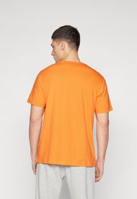 Orange Baumwoll-T-Shirt mit kurzen Ärmeln und Rundhalsausschnitt, mit lockerer Passform und glatter Textur. Kombiniert mit grauen Jogginghosen.