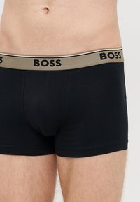 Μαύρα ανδρικά μποξεράκια με αντίθετη μπεζ μέση που φέρει το λογότυπο «BOSS» σε μαύρο χρώμα. Ομαλό ύφασμα και εφαρμοστό σχέδιο με κοντά πόδια.