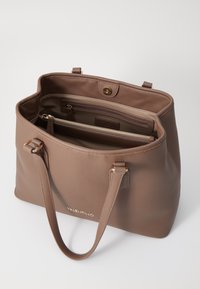 Braune Leder-Tote mit strukturierten Oberflächen, zwei Griffen, einer Reißverschlussinnentasche und einem magnetischen Druckverschluss. Goldenes Logodetail.