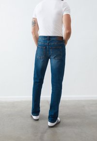 Tmavě modré džínové kalhoty s úzkým střihem. Mají dvě zadní kapsy, koženou nášivku v oblasti pasu a bílé tenisky s černými pruhy.