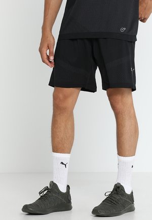 Czarne sportowe szorty o teksturowanym wzorze, w połączeniu z białymi skarpetkami i ciemnozielonymi butami sportowymi. Szorty mają luźny krój i długość do kolan.