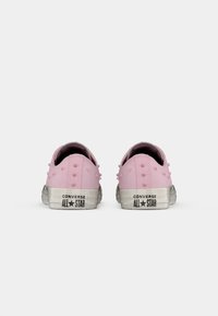 Rosa lærretssko med en myk tekstur, dekorative pigger og en hvit gummisåle med "Converse All Star" merke.