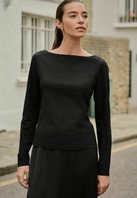 Black long-sleeve top with a wide boat neckline, fitted silhouette, and smooth texture, paired with a matching black skirt.