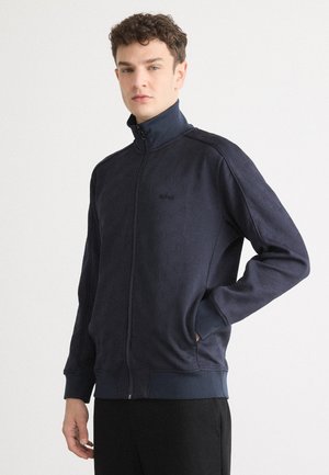 Donkerblauwe zip-up jack met een gemêleerd patroon, hoge kraag en zijzakken. Bevat een embleem op de borst en ribgebreide manchetten.