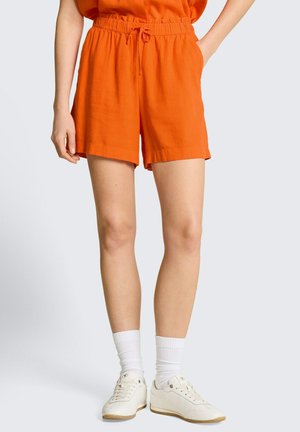 Persoon die feloranje shorts met trekkoord draagt, witte enkelsokken en witte vetersneakers tegen een effen lichte achtergrond.