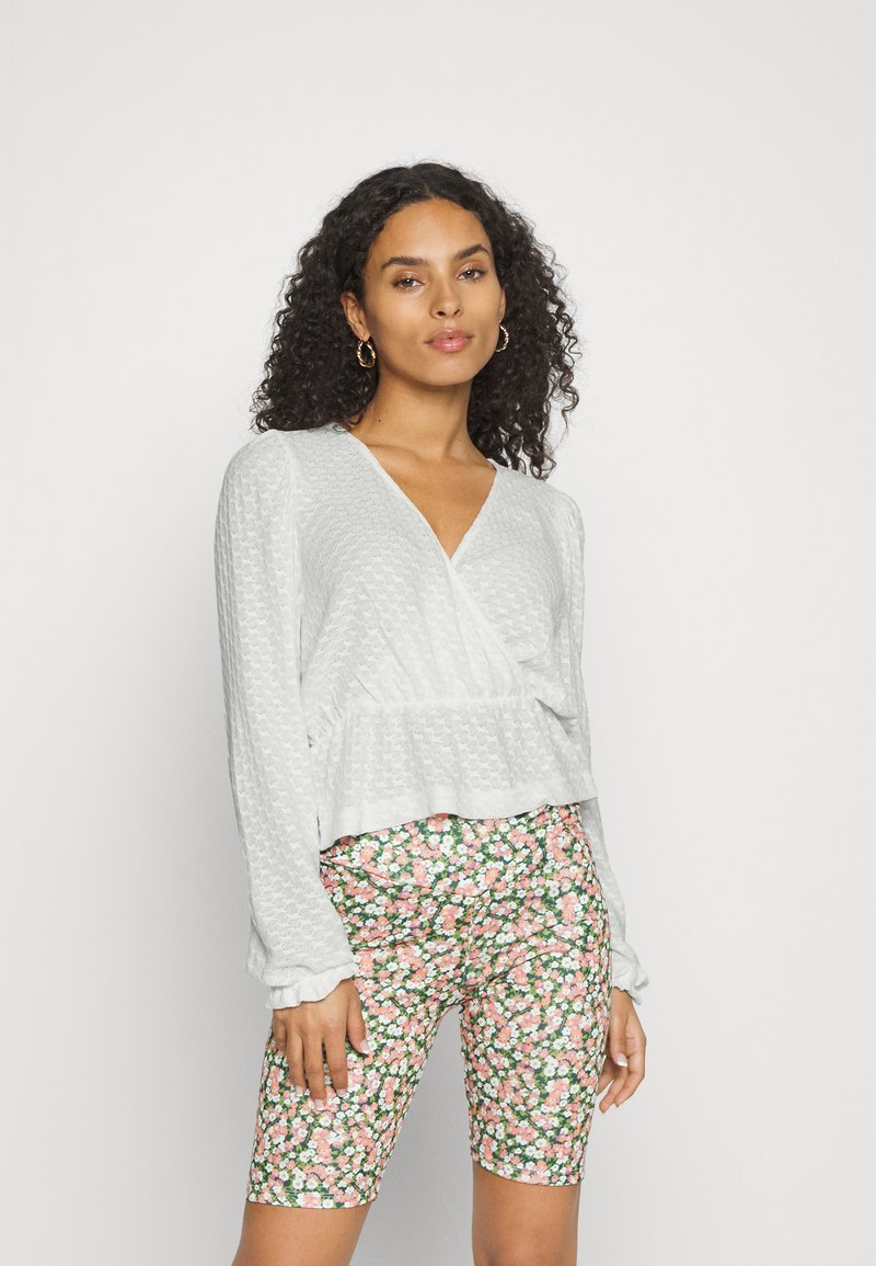 Top envolvente em cinza claro texturizado com mangas compridas, combinado com calções de cintura alta com um padrão floral em rosa e verde.