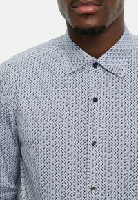 Hellblaues Hemd mit Kragen und geometrischem Muster in Dunkelblau und Hellbraun. Glattes Material mit klassischer Passform.