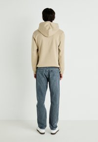 Sudadera con capucha beige de corte relajado, combinada con jeans de color azul claro y zapatillas blancas. Diseño minimalista sin logos visibles.