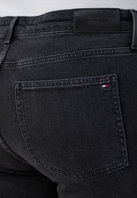 Jeans in denim nero con un design a vita media, tasche posteriori e un'etichetta in pelle Tommy Hilfiger in vita. Dettagli di cucitura sottili.