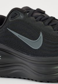 Chaussure de course noire Nike avec logo swoosh gris, empeigne en mesh et semelle épaisse rembourrée.