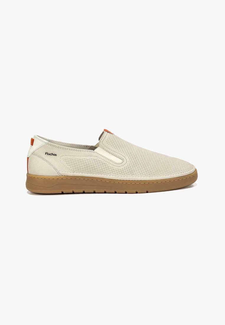 Zapatos slip-on con una parte superior de piel perforada beige, acento naranja en contraste y una suela de goma marrón claro, presentando una textura suave y un diseño minimalista.
