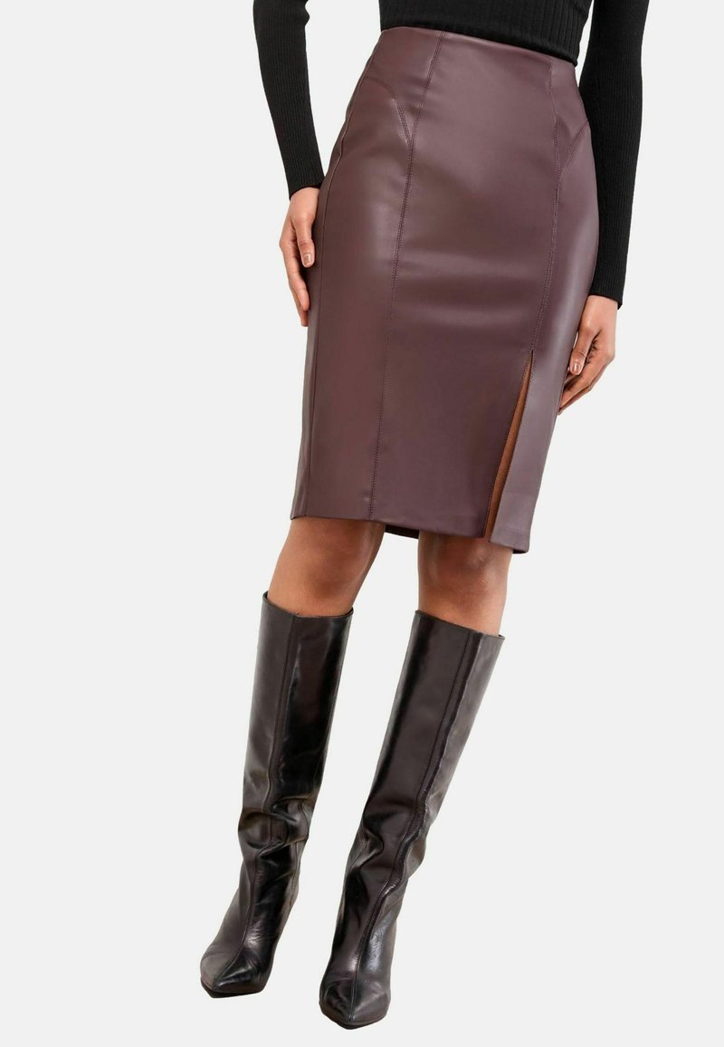 Fustă creion din piele ecologică maro cu o despicătură pe lateral, având o textură netedă și un design ajustat. Asortată cu cizme negre din piele, până la genunchi.
