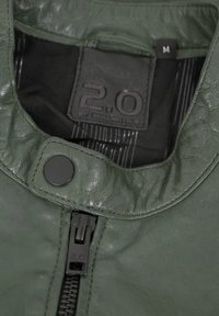 Grüne Lederjacke mit glatter Textur, Stehkragen und schwarzem Reißverschluss. Verfügt über einen runden Druckknopfverschluss und ein inneres Etikett mit der Beschriftung "M".