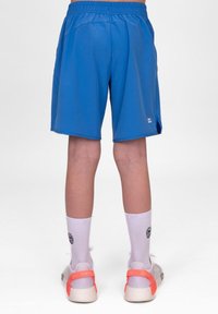 Blaue Sportshorts mit einem elastischen Bund, Seitentaschen und lockerer Passform. Getragen mit weißen Socken und Turnschuhen mit orangen Akzenten.