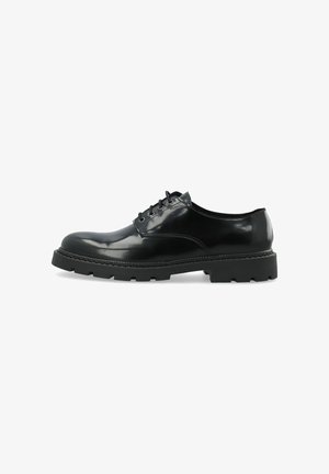 Zapato de vestir de cuero negro con cordones, suela gruesa y texturizada y acabado pulido y liso, mostrado de lado sobre fondo blanco.