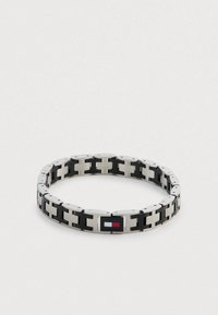 Metalowa bransoletka z naprzemiennymi srebrnymi i czarnymi ogniwami, z prostokątnym zapięciem ozdobionym logo w kolorach czerwonym, białym i niebieskim.