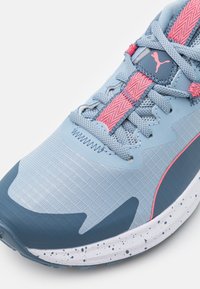 Scarpa sportiva azzurro chiaro con accenti blu scuro in contrasto, superiore testurizzato, lacci rosa e suola bianca punteggiata.