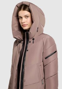 Puffer jacket in soft pink with a large hood, side pockets, and black zipper details. Features a quilted texture with horizontal stitching.