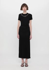 Black maxi dress with short sleeves, smooth fabric, a fitted bodice, and a chain detail at the neckline. Paired with strappy black sandals.