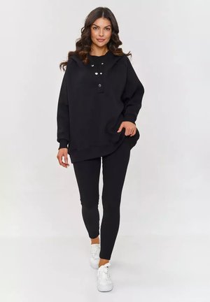 Czarny oversize sweter z guzikami, w zestawie z czarnymi legginsami i białymi sneakersami. Gładki materiał o luźnym kroju.