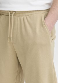 Beige cotton sweatpants with an elastic waistband and drawstring, featuring side pockets and a soft, smooth texture.