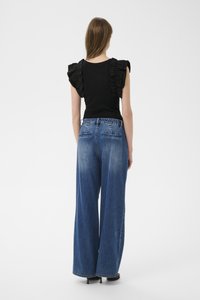 Čierny top s volánikmi na ramenách v kombinácii so širokými, vyblednutými modrými džínsami. Jednoduchý dizajn s hladkou textúrou a klasickým strihom.
