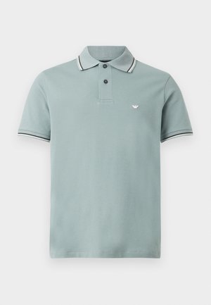 Lichtblauw poloshirt met korte mouwen, twee zwarte knopen, gestreepte kraag en mouwranden, en een klein wit logo op de linkerborst.