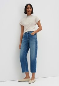 Beige gestreepte korte mouwen top, hoog-gewaste lichtblauwe jeans en crèmekleurige platte schoenen. Gladde texturen met een ontspannen pasvorm.