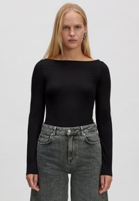 Schwarzer Langarm-Body mit U-Boot-Ausschnitt, kombiniert mit hochgeschnittenen grauen Jeans aus Denim, die eine ausgebleichte Textur und seitliche Taschen besitzen.