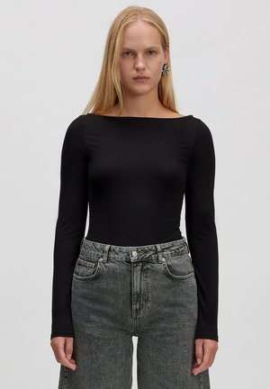 Schwarzer Langarm-Body mit U-Boot-Ausschnitt, kombiniert mit hochgeschnittenen grauen Jeans aus Denim, die eine ausgebleichte Textur und seitliche Taschen besitzen.