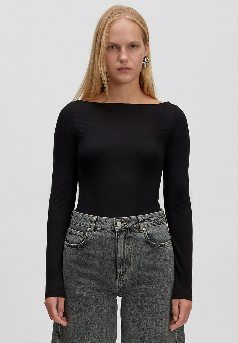 Schwarzer Langarm-Body mit U-Boot-Ausschnitt, kombiniert mit hochgeschnittenen grauen Jeans aus Denim, die eine ausgebleichte Textur und seitliche Taschen besitzen.