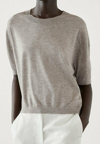 Vaaleanharmaa lyhythihainen neulepusero pehmeästä neulemateriaaliesta, pyöreä pääntie, rento malli, ribbaatut hihat ja helma, yhdistetty valkoisiin housuihin.