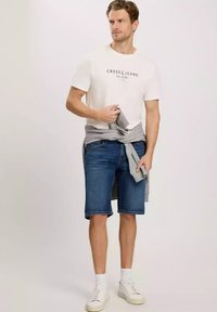 Biała koszulka z krótkim rękawem z napisem, niebieskie szorty dżinsowe i białe trampki. Szary sweter związany w pasie. Niezobowiązujący strój.