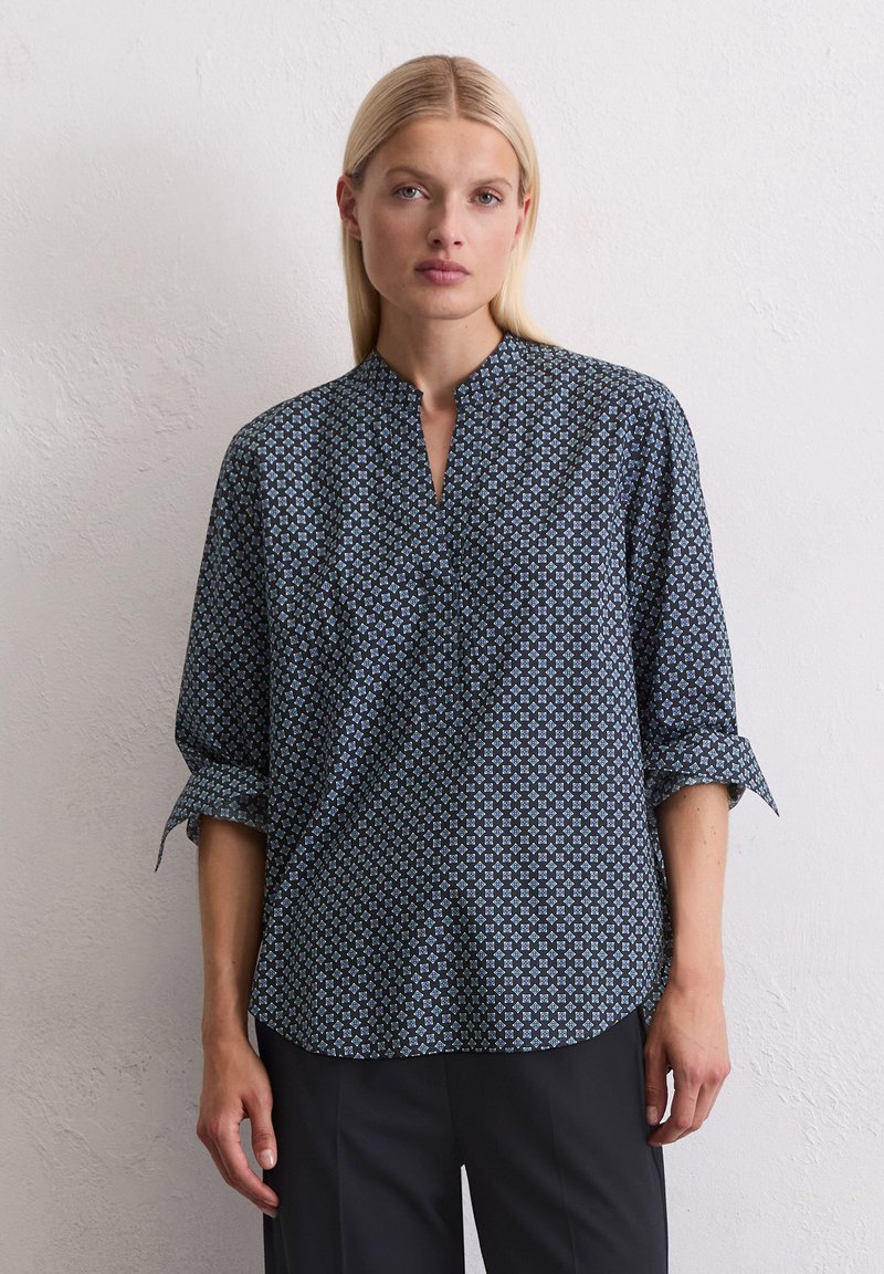 Zwarte en blauwe gebloemde blouse met een staande kraag, lange mouwen opgerold en een relaxte pasvorm. De stof lijkt lichtgewicht en soepel.