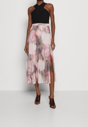 Sukienka plisowana z czarnym prążkowanym gorsetem i kwiatową różowo-fioletową spódnicą z rozcięciem do uda, zestawiona z brązowymi butami na otwartym palcu.